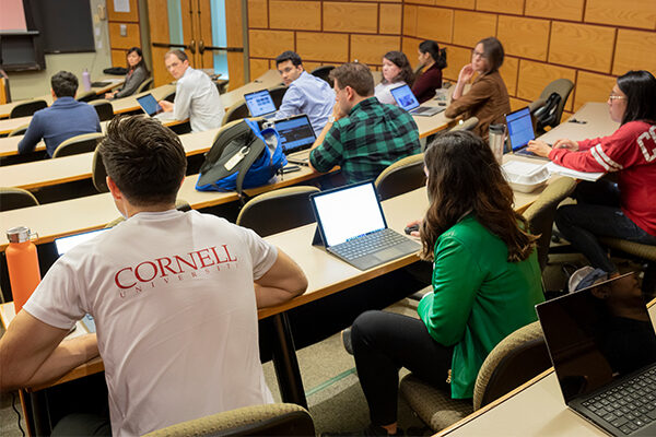 Students sit in a tiered classroom with laptop open in front of them.